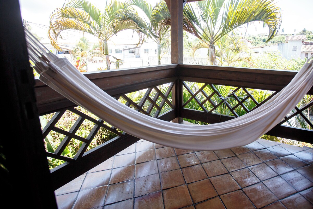 A hammock on a wooden balcony with a tiled floor, surrounded by a lattice railing.