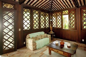 Una habitación con techo de madera, un sofá con tapicería floral, una mesa con velas y un diseño de ventana en celosía.