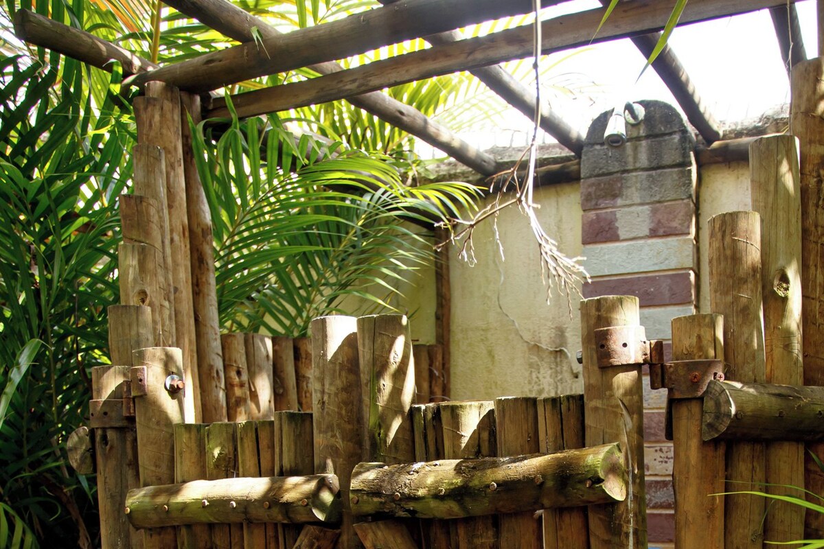 A rustic wooden fence with a simple crossbeam structure, surrounded by greenery and a stone-paved area.