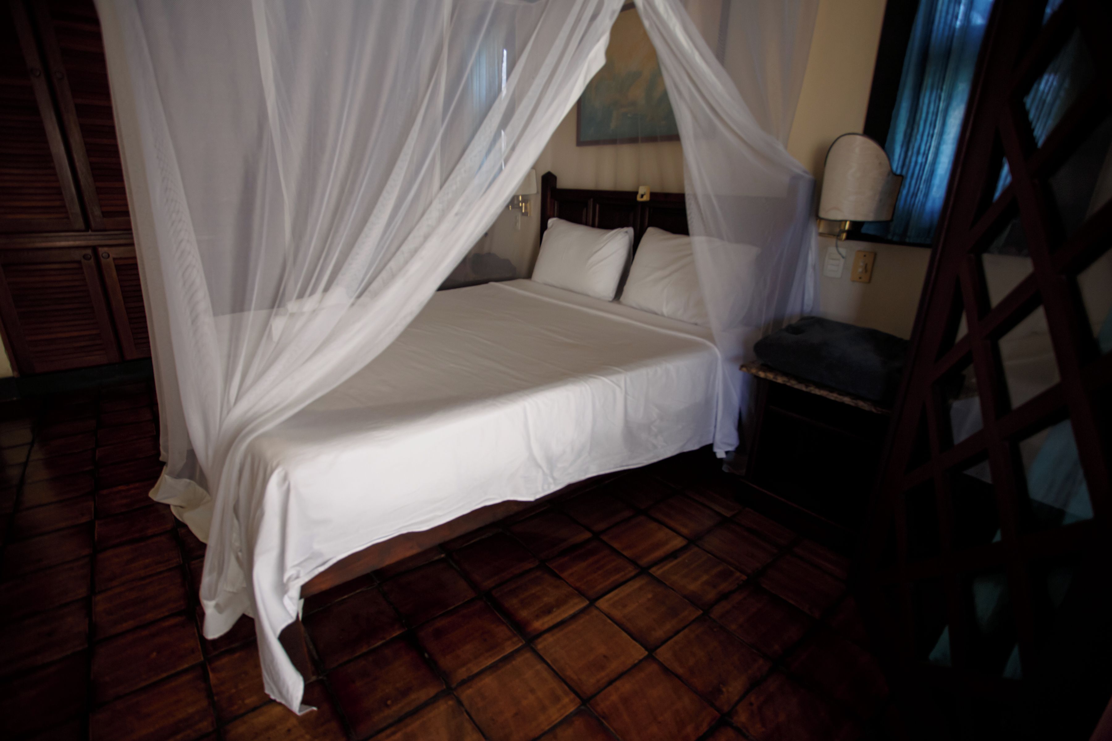A bed with a canopy, a nightstand, a lamp, and a wooden floor.