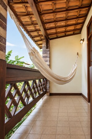 A hammock hanging between wooden beams on a balcony with a tiled floor and a lattice railing. - Pousada Rosa dos Ventos (Porto Seguro)