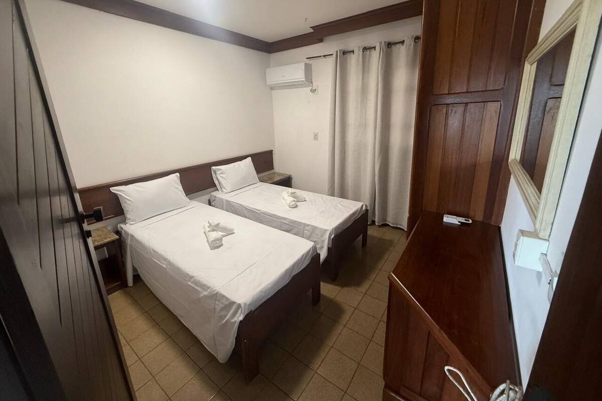 Ein Hotelzimmer mit zwei Betten, einem Holzschrank, einem kleinen Tisch und einer Klimaanlage.