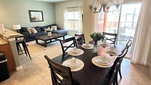 A dining area with a table set for four, a sofa, and a window with curtains. - Lake View Private Pool Townhome - Sleeps 10 (Kissimmee)