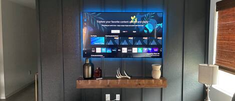 Una sala moderna con televisor montado mostrando una interfaz de Smart Hub, una consola de madera y un sofá.