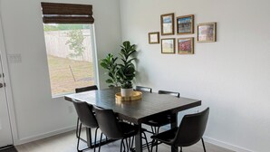A dining area with a table, chairs, a potted plant, and framed pictures on the wall.