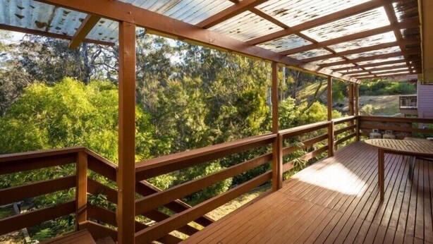 Eine Holzterrasse mit Metallveranda, umgeben von viel Grün.