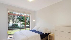 Ein Schlafzimmer mit Bett, Nachttisch, Schminktisch und einer Schiebetür zum Balkon.