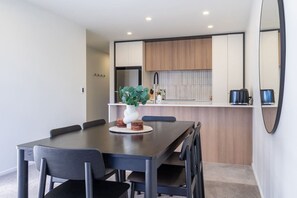A modern dining area with a dark wooden table, black chairs, and a vase with green leaves. - Premium Colombo Townhouse - CBD + Private Garage (Christchurch)