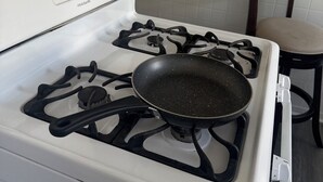 A kitchen with a white stove, a frying pan on the burner, a chair, and a small orange bowl on the counter.