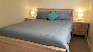 Ein Einzelbett mit Holz-Kopfteil, zwei Nachttische mit Lampen und eine Wand in neutraler Farbe.