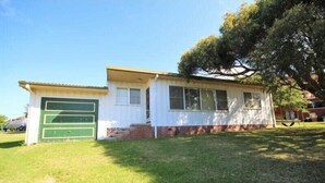 Einbungalow mit Garage, einer Veranda und einem großen Baum im Hintergrund.