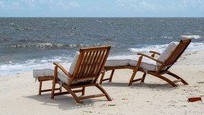 Deux chaises de plage en bois sur une plage de sable, avec l’océan en arrière-plan.