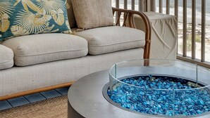 Une pièce avec un canapé beige, une table basse en verre ornée de motifs bleus, une vue sur l’océan et une rambarde en bois.