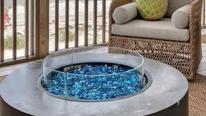 Un balcon doté d’une table à plateau en verre, de meubles en osier et offrant une vue sur la plage.