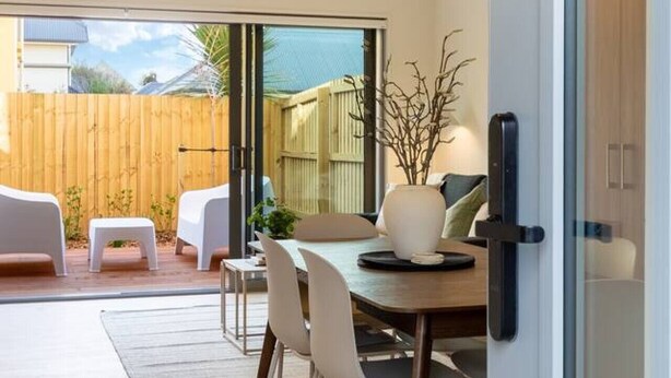 A modern dining area with a glass door leading to a patio, a wooden fence, and a view of the sea.