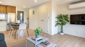 A modern living room with a dining area, a kitchen, and a TV mounted on the wall.