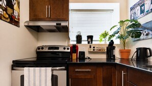 A kitchen with a stove, oven, wooden cabinets, a window with blinds, a potted plant, and a coffee maker. - Heart of Corydon (Winnipeg)
