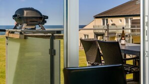 Vista desde un balcón con una parrilla, sillas de mimbre y una mesa con copas de vino.