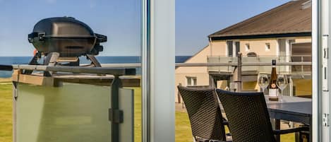 A view from a balcony with a grill, wicker chairs, and a table with wine glasses.