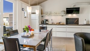 Una cocina moderna con armarios blancos, una mesa de comedor con sillas, un televisor sobre la encimera y vistas al exterior.