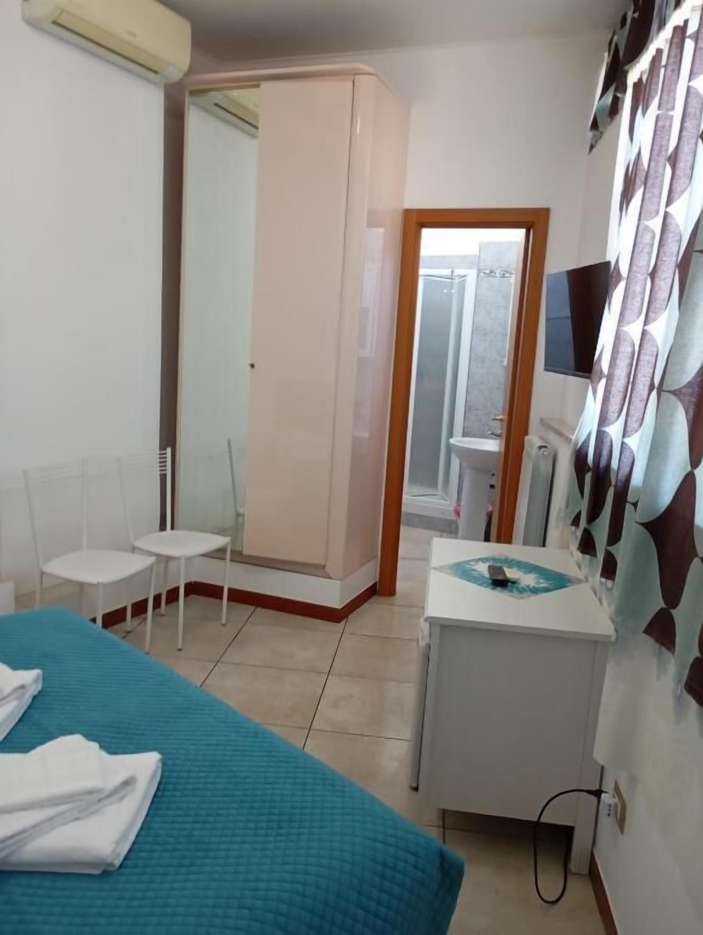 A hotel room with a bed, a desk, a chair, a mirror, and a television.