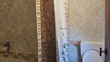 Un baño con inodoro, cortina de ducha y pared de azulejos.