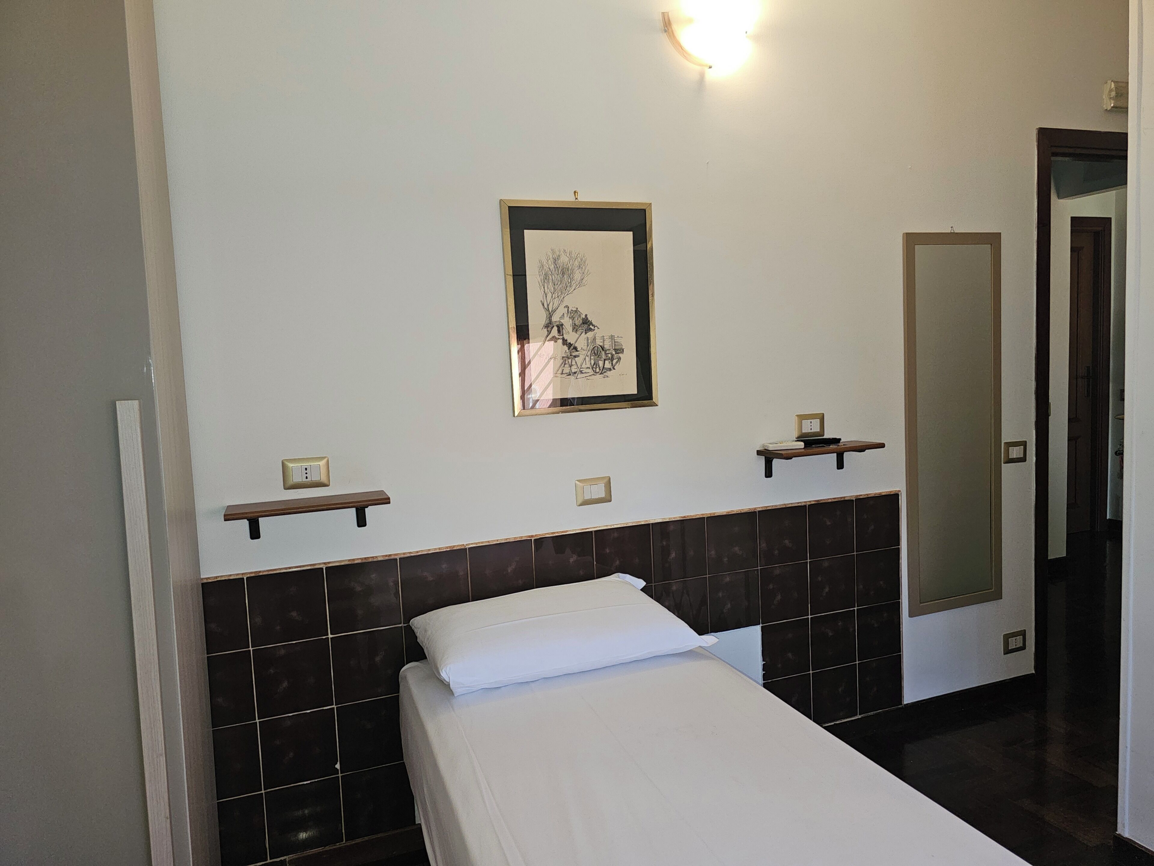 Une chambre d’hôtel avec un lit, un tableau encadr é au mur, une petite étagère et un miroir.