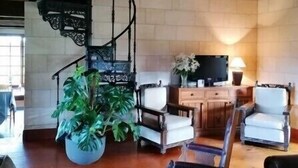 Amplia sala de estar con una escalera de caracol, asientos cómodos, una planta grande en maceta y un televisor.
