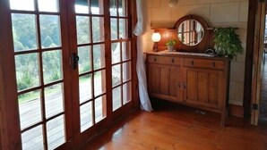 Un armario de madera con espejo y lámpara, una cortina, y vista a follaje verde a través de una puerta de cristal.
