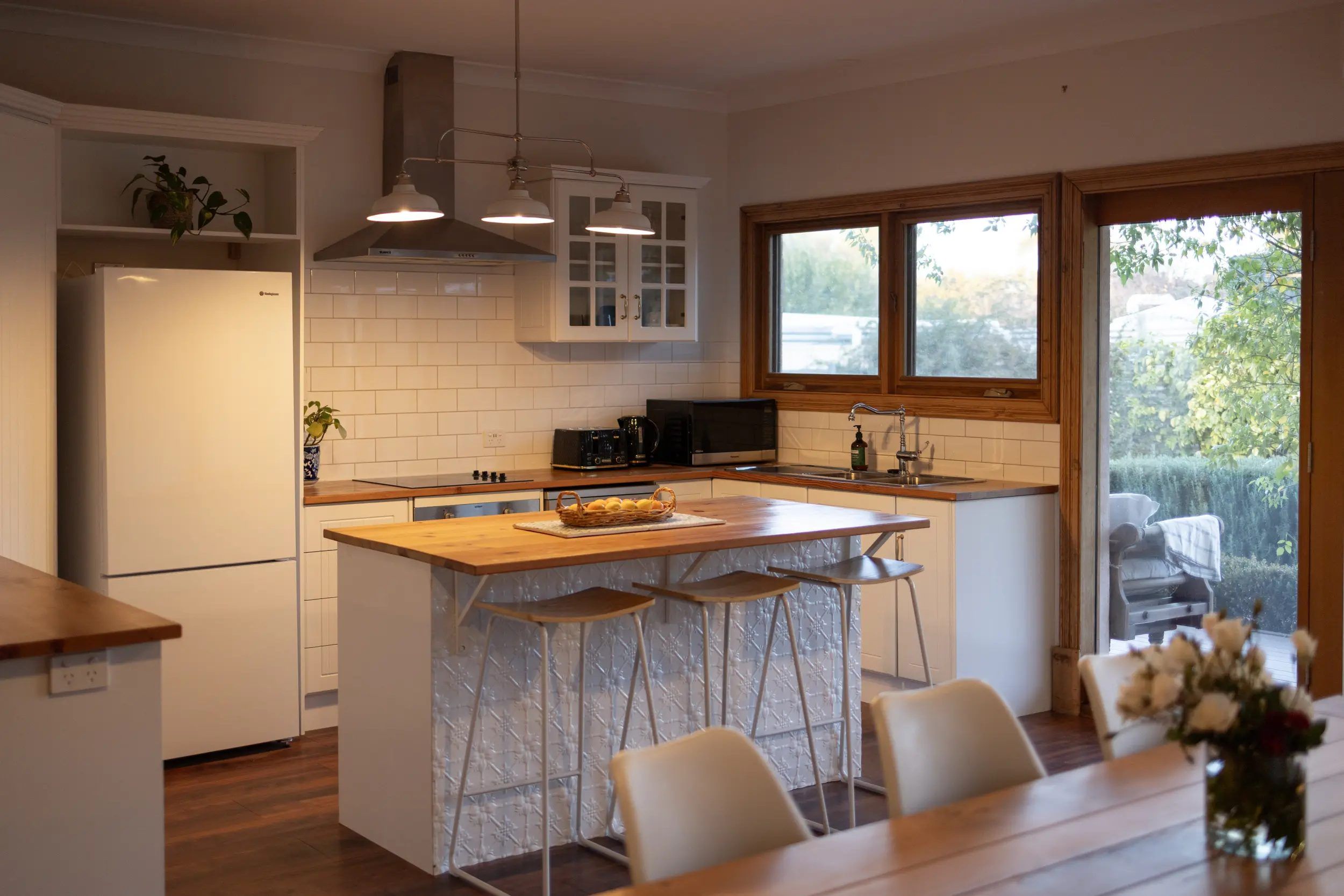 Cozinha moderna com ilha central, banquetas, geladeira e janela com vista para o exterior.