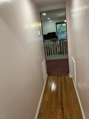 Um corredor com piso de madeira, paredes brancas e vista para uma varanda com guarda-corrimão.