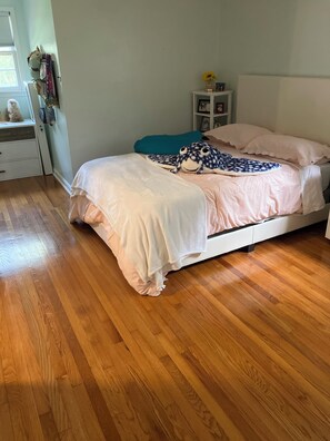 Quarto com cama, mesa de cabeceira, cômoda e janela.