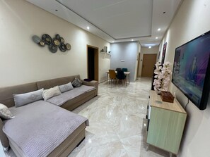 Een moderne hotelkamer met een slaapbank, een eethoek en een aan de muur bevestigde televisie.