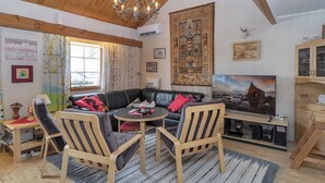 Un salon chaleureux avec un plafond en bois, un canapé en cuir noir, des fauteuils à rayures, une table basse ronde et un grand tableau accroché au mur.