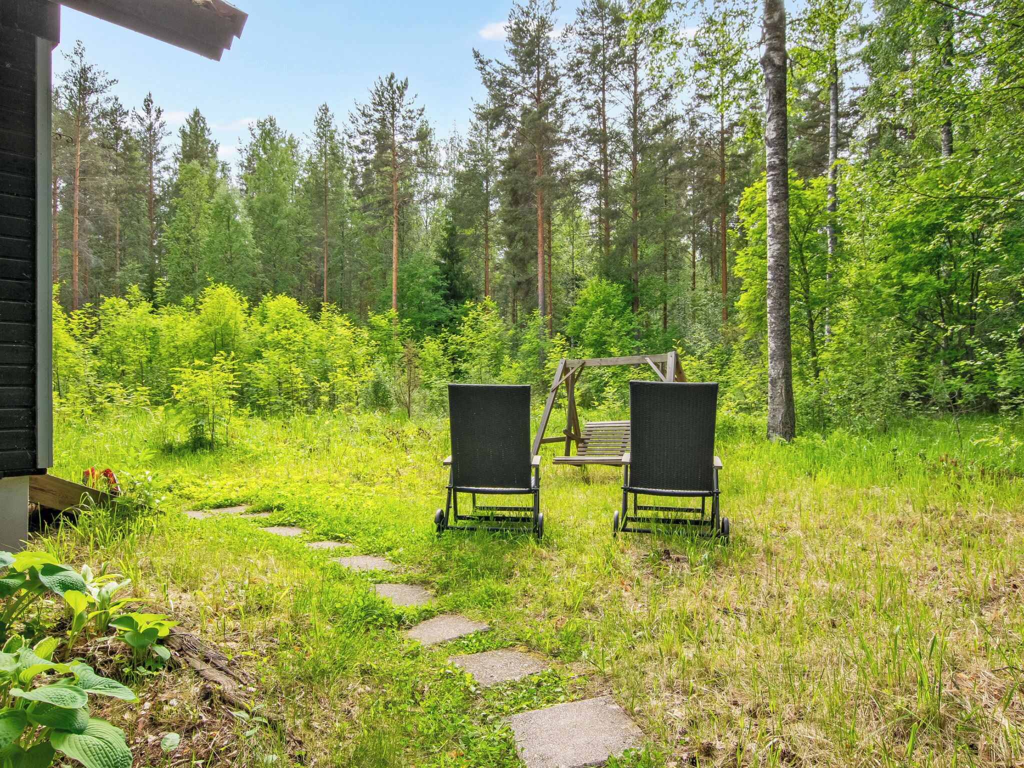 A wooden deck with two black chairs and a swing set in a forested area.