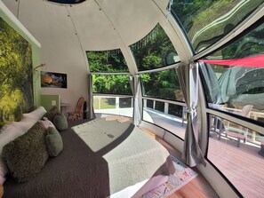 A room with a bed, a chair, a large window, and a view of greenery outside. - Exclusive Private Woodland Escape – Book 2 domes on 100+ Acres (Milledgeville)