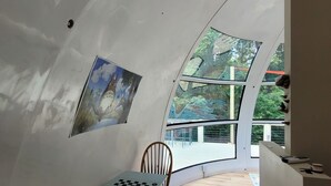 A room with a curved ceiling, a chess table, a wooden chair, and a painting on the wall.