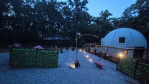 A gravel pathway leading to a gazebo, a dome structure, and a hedge with flowers.
