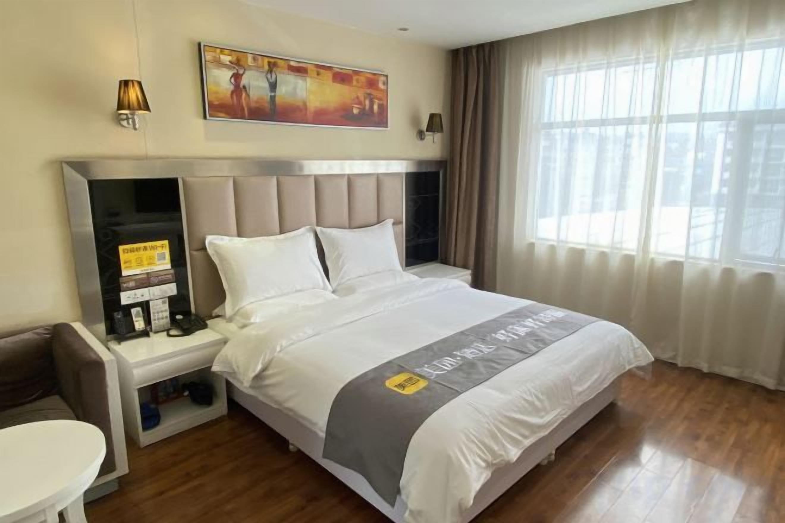 A hotel room with a bed, a desk, a chair, a nightstand, and a window with curtains.