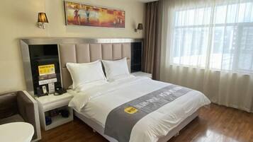 A hotel room with a bed, a desk, a chair, a nightstand, and a window with curtains.