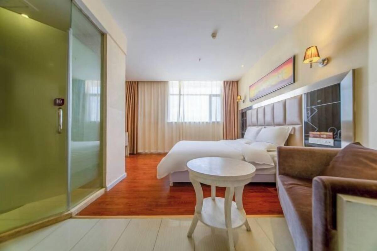 A hotel room with a bed, a sofa, a small table, and a sliding glass door.