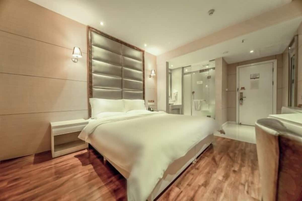 A modern hotel room with a large bed, bedside tables, a mirror, and a shower area.