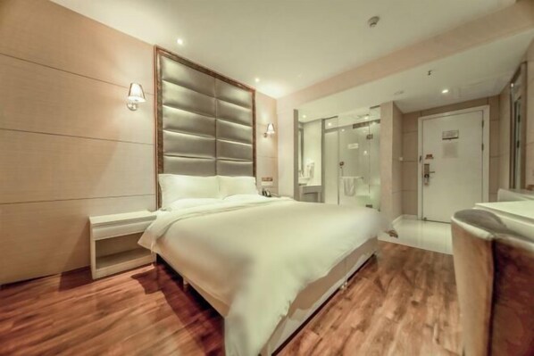 A modern hotel room with a large bed, bedside tables, a mirror, and a shower area.