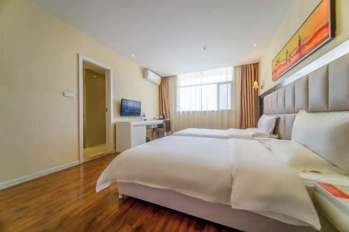 A hotel room with a bed, a desk, a television, and a window with curtains.