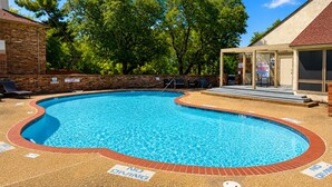A swimming pool with a brick border, surrounded by a brick wall and trees. - Modern 2BR Condo, Fast Wi-Fi, Blackout Draperies (Irving)