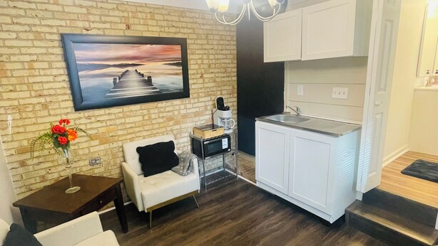 A modern living room with a brick wall, a white sofa, a coffee table, and a dining area with white cabinets and a kitchen island.