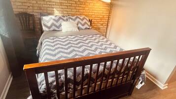 Een slaapkamer met een bakstenen muur, een bed met houten hoofdeinde, een vloerlamp en een bordje aan de muur.