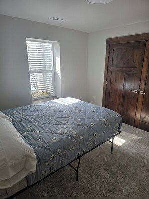 A bedroom with a bed, a window with blinds, a wooden door, and a carpeted floor. - Brand new peaceful 3-bedroom townhome with AC in charming Helena (Helena)
