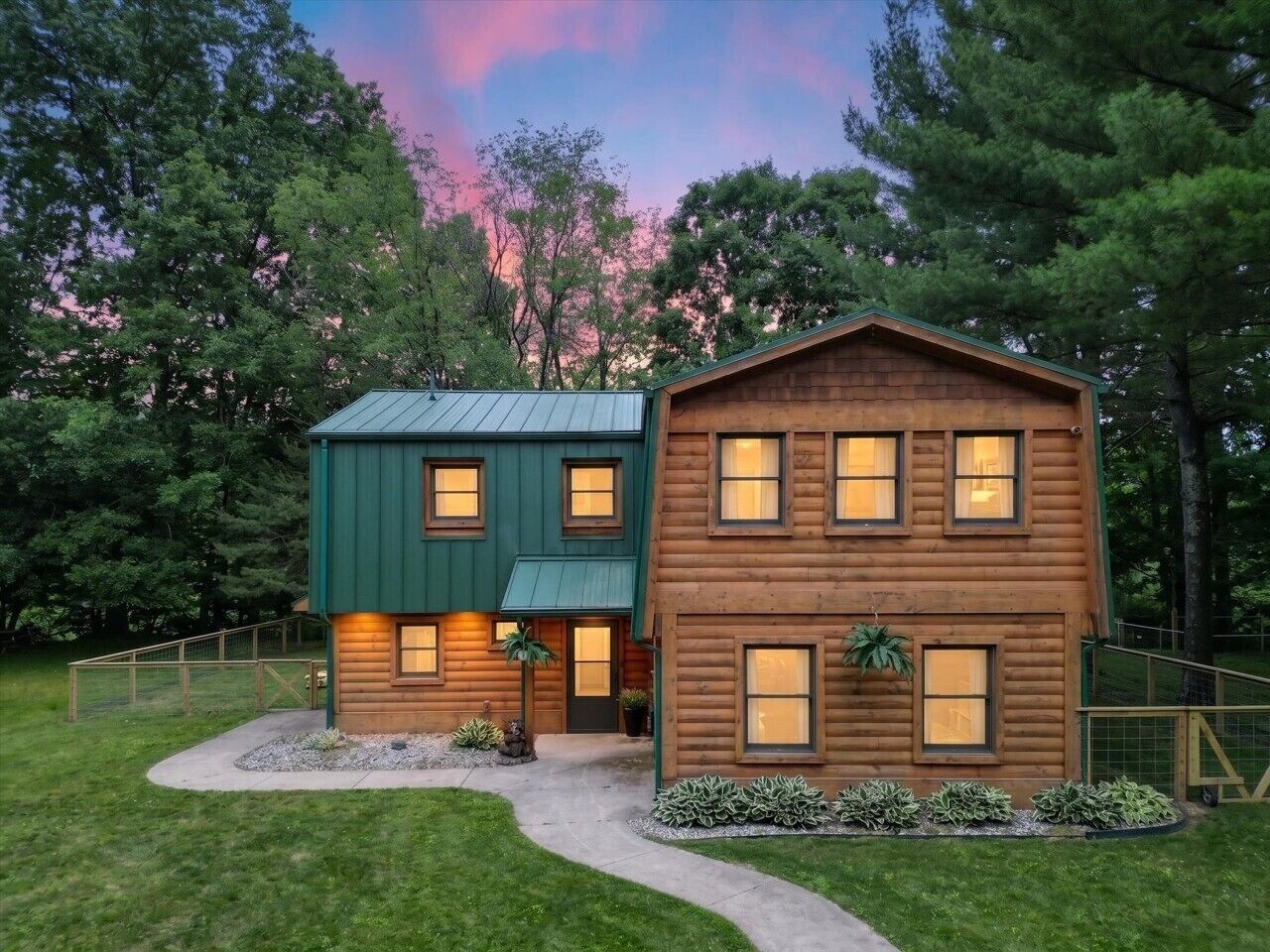 A two-story log cabin with a green roof, a front porch, and a landscaped yard.