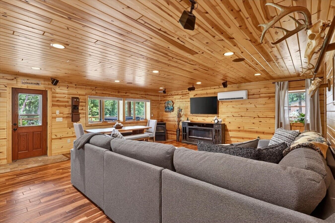 A log cabin interior with a sectional sofa, a fireplace, a television, and wooden walls.